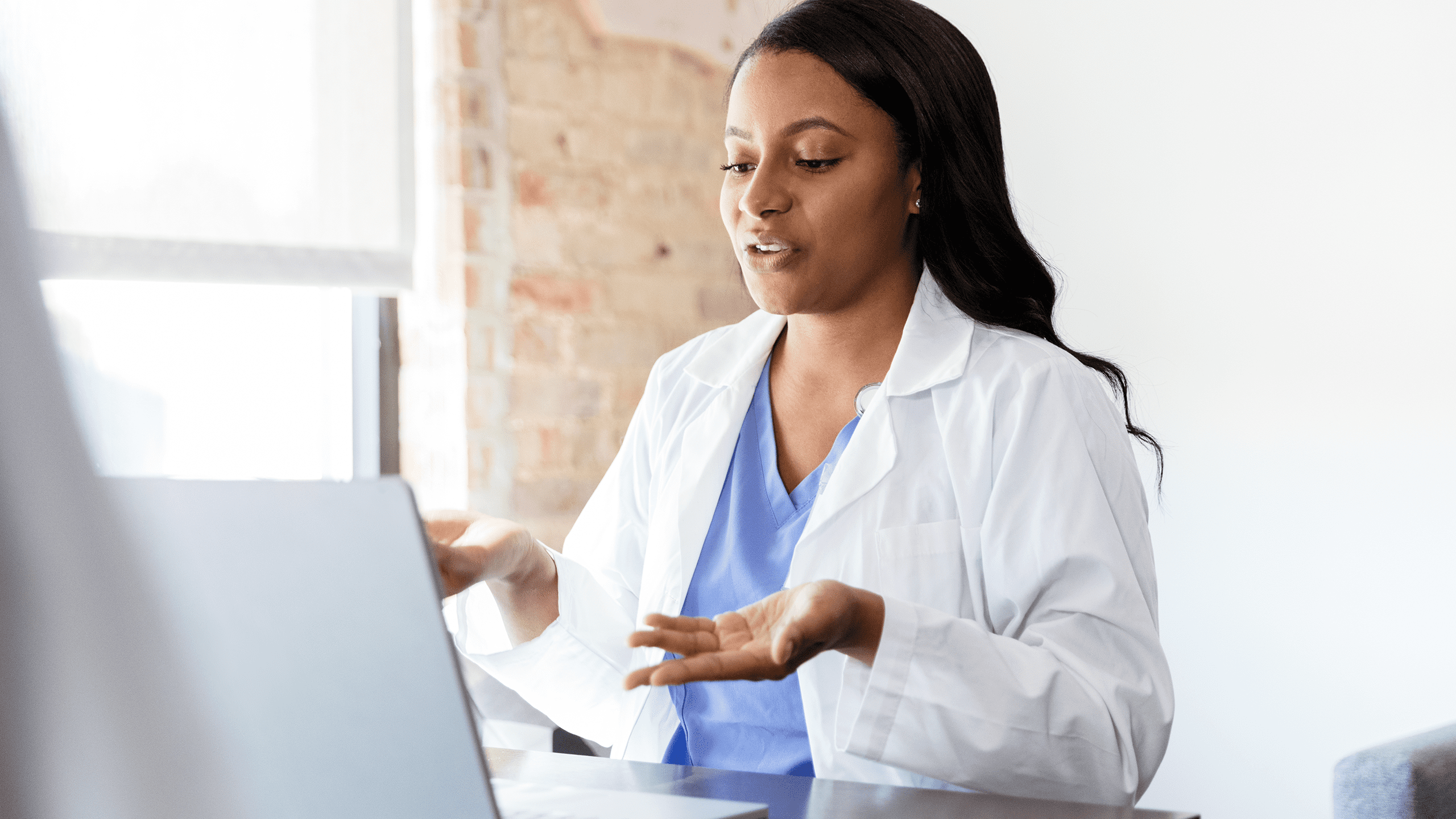 A woman in a white coat collaborating virtually via her laptop